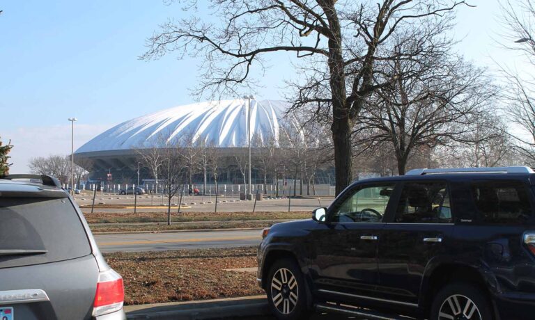 The photo shows a gray car and a blue car, with a university sports stadium in the background.