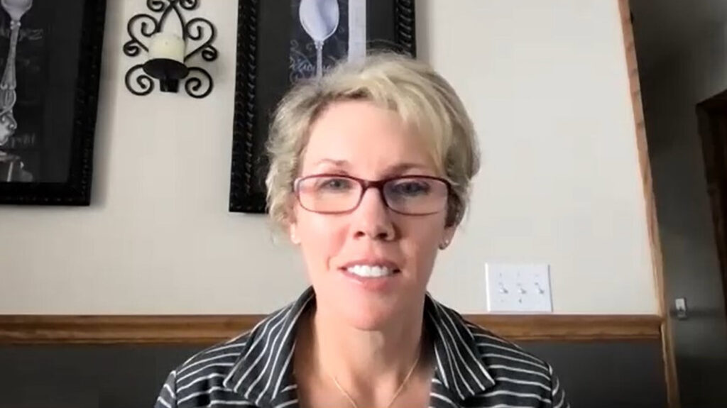 A woman with glasses smiles from her living room.