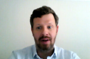 A man looks at his webcam, in front of a white background.