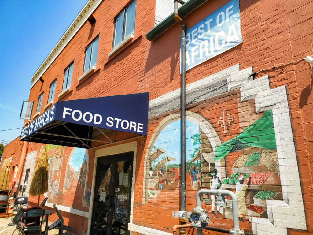 The image shows a red brick building with murals and a blue shade over the entrance that reads "Best of Africa Food Store."